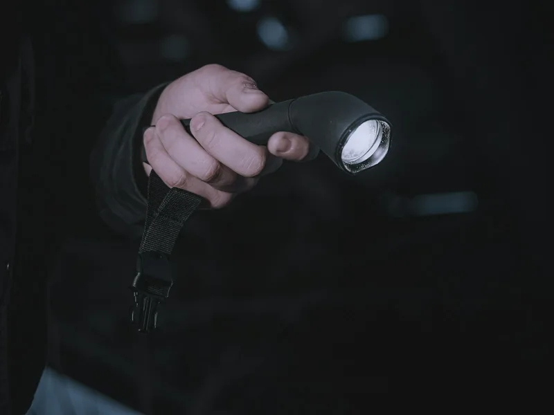 Main d'agent de sécurité tenant une lampe torche allumée dans l'obscurité, levée de doute nocturne sur alarme