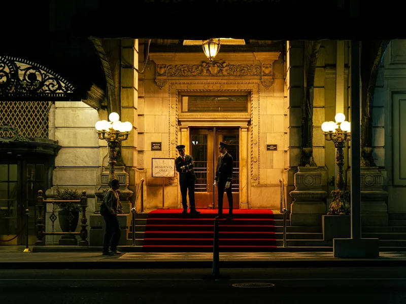 Agents de sécurité en uniforme devant l'entrée illuminée d'un grand hôtel de luxe avec tapis rouge, de nuit